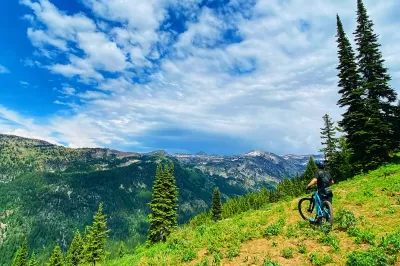 SKI IDAHO THIS SUMMER : A mountain biker takes a break from the trail last summer to enjoy Grand Targhee Resort's breathtaking views. Eleven of Idaho's 19 ski areas offer mountain biking in the summer, as well as scenic chairlift and gondola rides, hiking and trail running, disc golf, zipline tours, horseback riding, and more. Visit skiidaho.us for more details. (Photo by Gary Peterson for Ski Idaho)